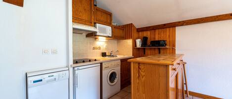 A compact kitchen with wooden cabinets, a dishwasher, a washing machine, and a microwave.