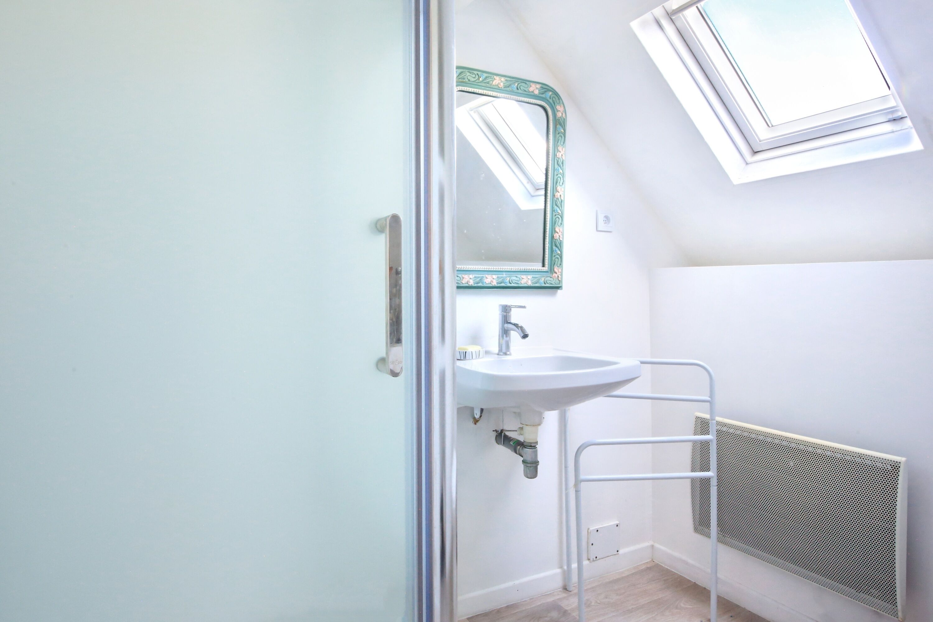 A bathroom with a white sink, a mirror with a decorative frame, a radiator, and a window providing natural light.