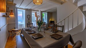 Un comedor con una mesa larga dispuesta para cuatro, sillas de madera, un florero con flores y una lámpara colgante.