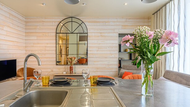Une cuisine moderne avec un mur en bois, un grand miroir et un coin repas agrémenté de coussins orange.