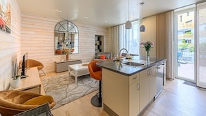 Une cuisine moderne dotée d’un îlot central, d’un coin repas avec une table blanche et des chaises orange, et d’une grande fenêtre offrant une vue sur l’extérieur.