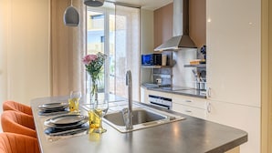 Une cuisine moderne dotée d’un îlot central, d’appareils électroménagers en acier inoxydable et offrant une vue sur l’extérieur.