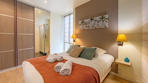 Une chambre d’hôtel comprenant un lit, deux lampes de chevet, un tableau, une armoire en bois et un espace douche.