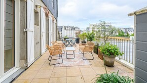 Un balcon avec des fauteuils en osier, une petite table et des plantes en pot.