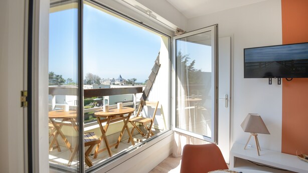 A modern room with a large sliding glass door leading to an outdoor dining area. - Chez Flora - Appartement pour 4 (Saint-Aubin-sur-Mer)