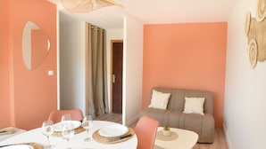 A dining area with a round table set for four, a sofa, and a small table with a plant. - Chez Flora - Appartement pour 4 (Saint-Aubin-sur-Mer)