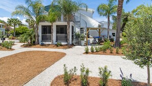 A modern two-story house with a covered patio, surrounded by a landscaped garden with various plants and a gravel driveway.
