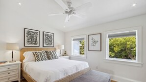 A bedroom with a bed, bedside tables, a ceiling fan, and framed artwork on the wall.