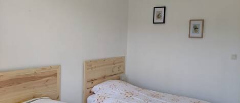 Een kleine kamer met een enkel bed, een houten hoofdbord, een wit sprei met bloemenprint en twee ingelijste foto's aan de muur.