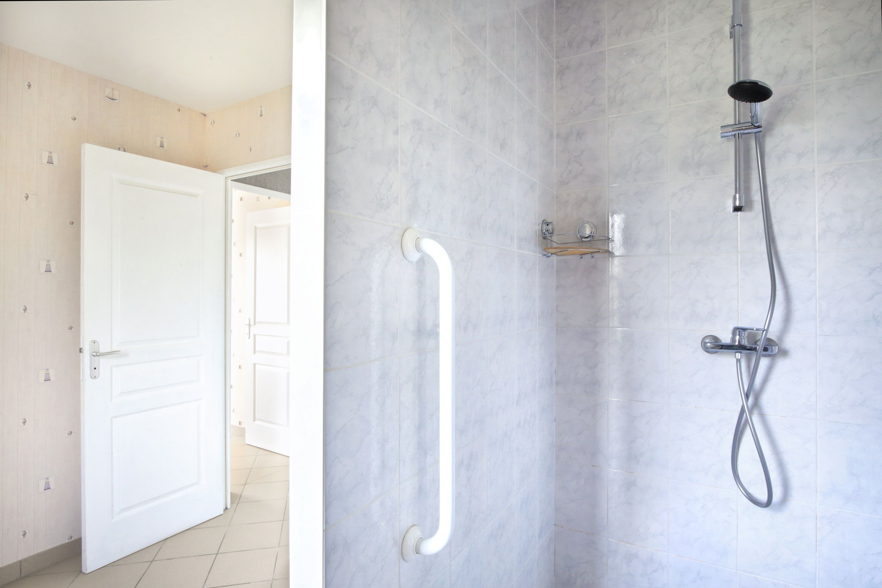 Een badkamer met een douche, een witte deur en een handgreep.