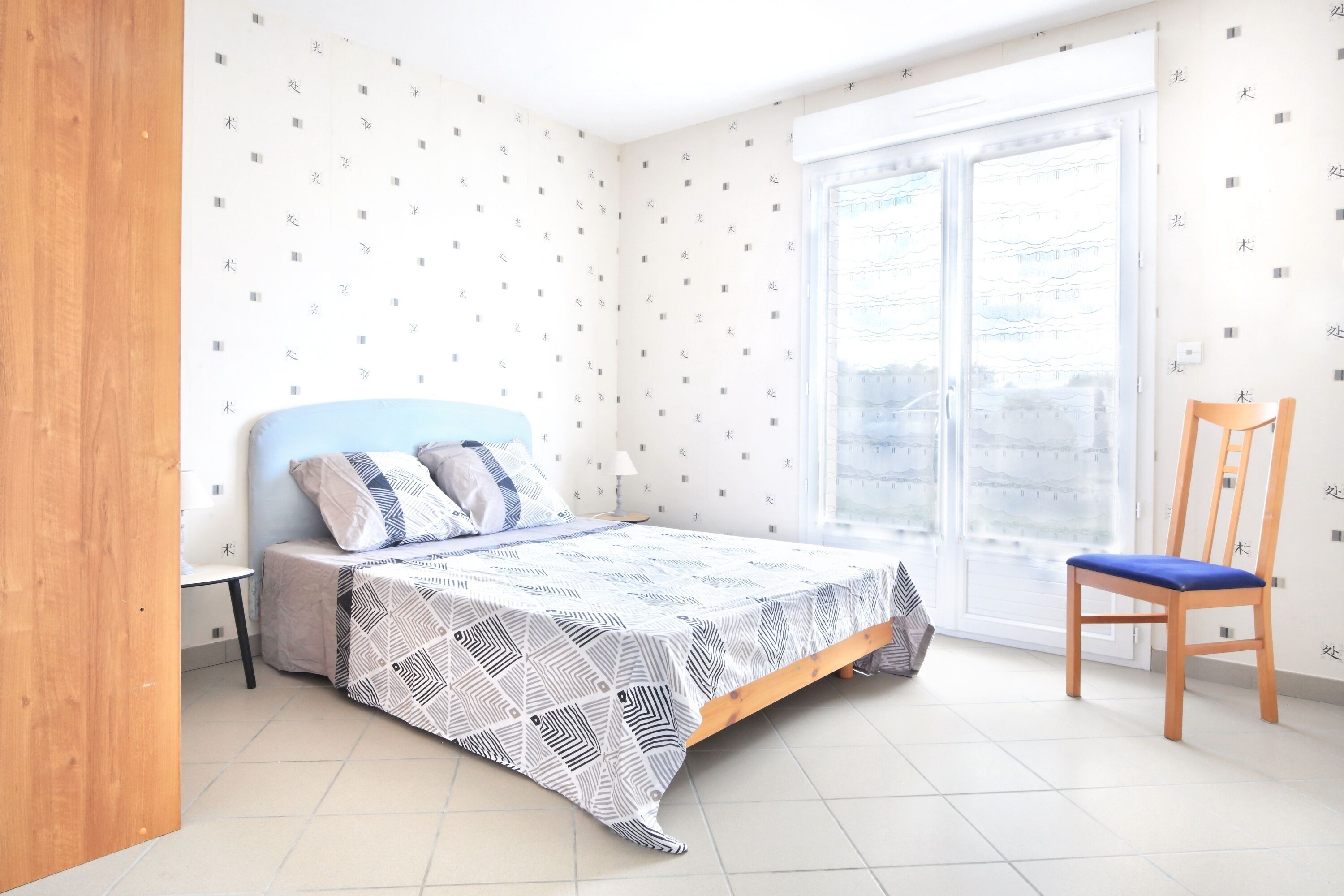 A bedroom with a bed, a chair, a small table, and a window with a view.