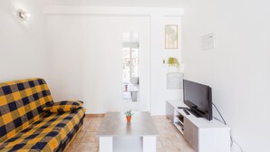 A living room with a checkered sofa, a coffee table with a plant, a TV on a white stand, and a door leading to a balcony.