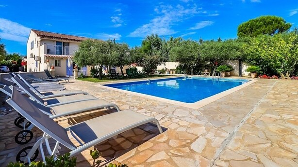 A swimming pool with lounge chairs, a building with a tiled roof, and surrounding greenery.