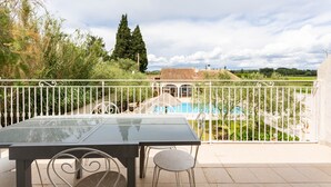 Ein Balkon mit Glastisch und Stühlen mit Blick auf ein Schwimmbad und Grünflächen.