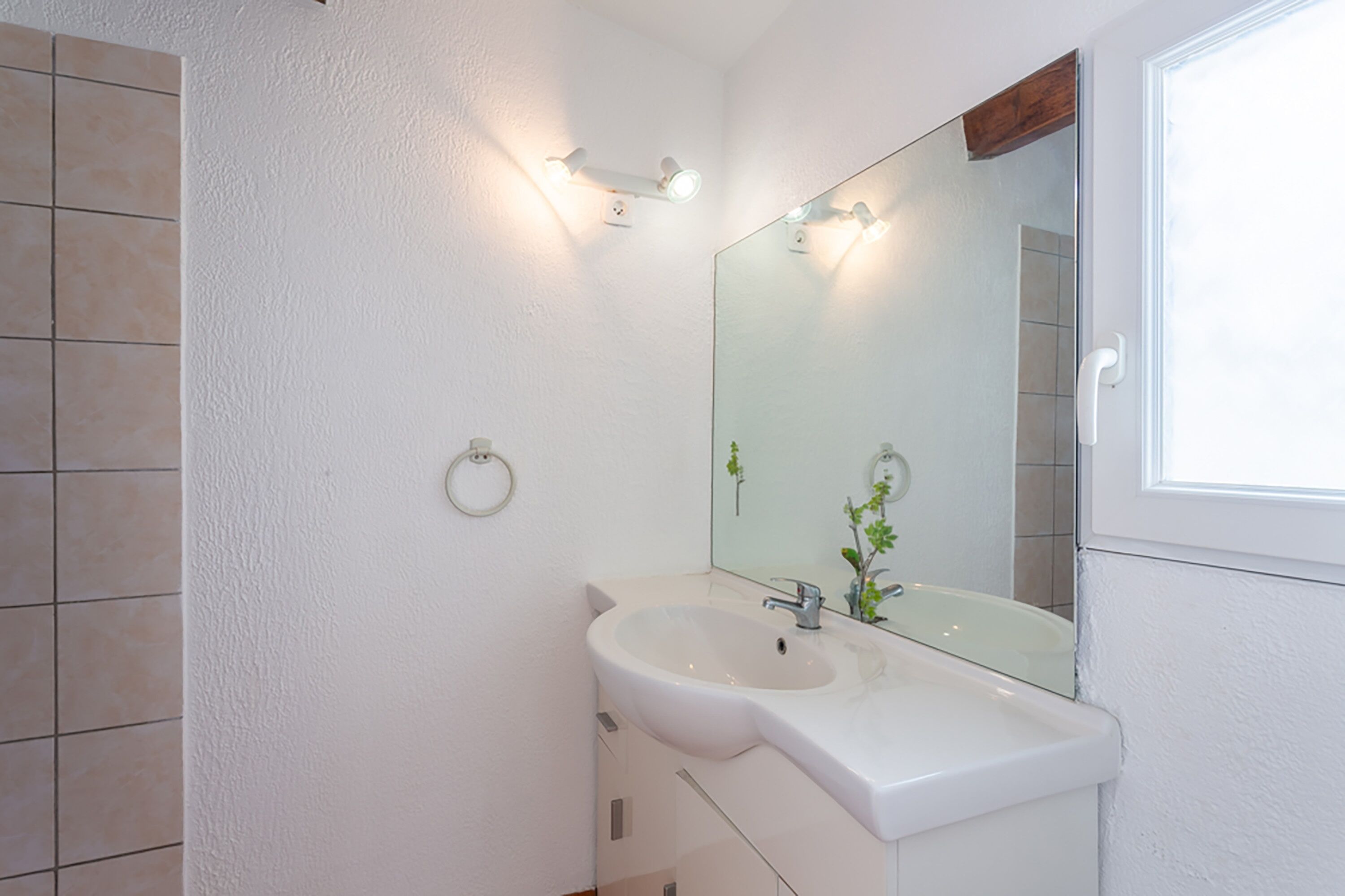 Ein Badezimmer mit weißem Waschbecken, einem Spiegel und einem Handtuchhalter an der Wand.