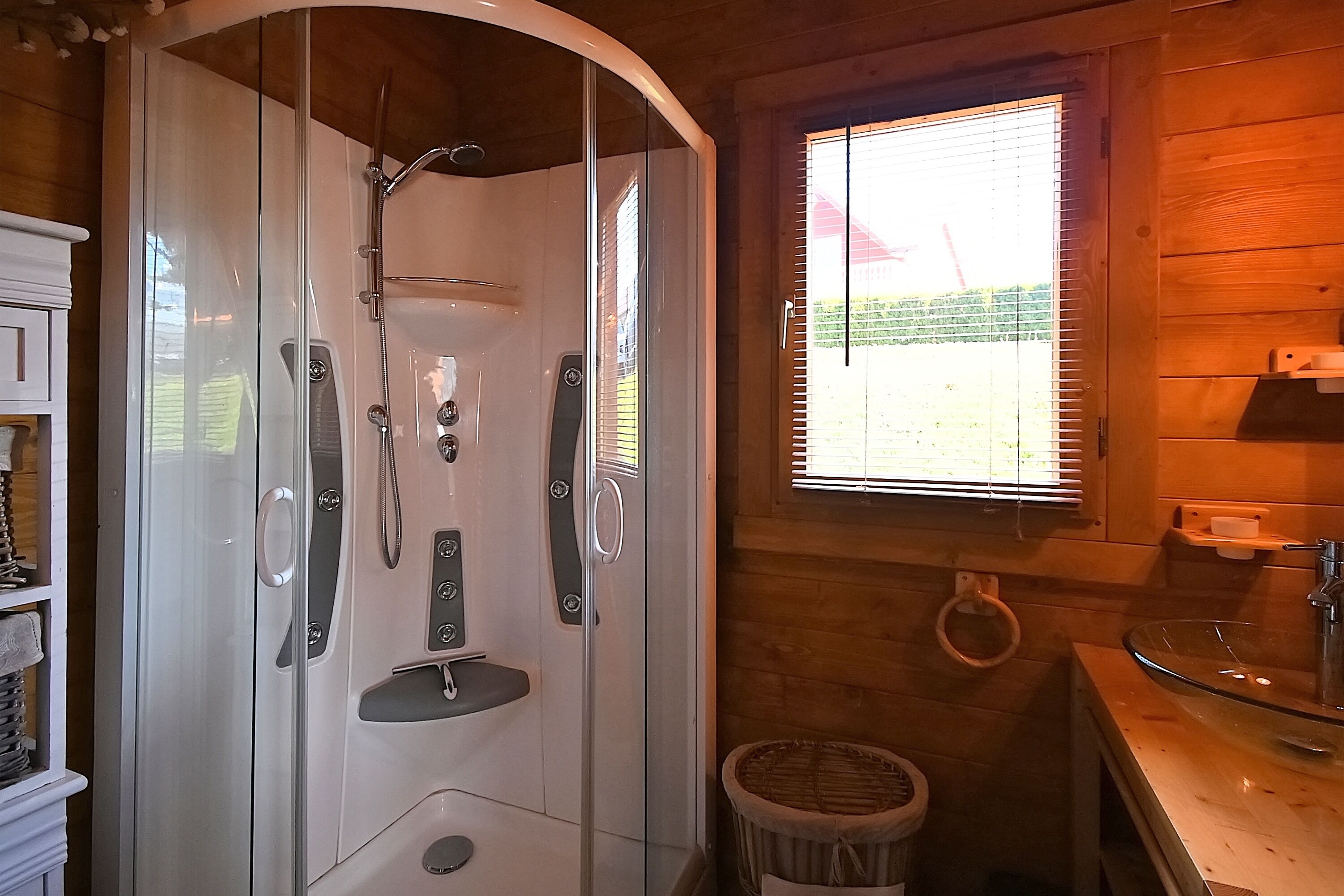 Een moderne badkamer met een douchecabine van glas, houten wanden, een wastafel en een raam met zonwering.