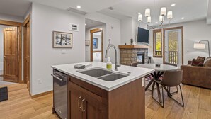 Uma cozinha moderna com ilha central, máquina de lavar louça embutida e área de jantar com mesa e cadeiras redondas.