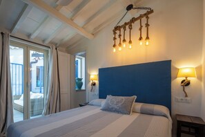 A bedroom with a bed, a blue headboard, two wall-mounted lamps, and a ceiling light fixture.
