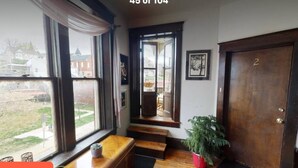 Una escalera conduce a un segundo piso con vistas a una zona residencial. Hay un banco al pie de la escalera, una planta en maceta a la derecha y una puerta con el número '2' también a la derecha.