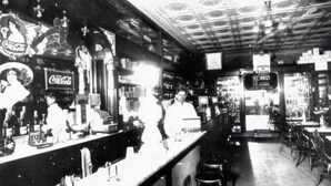 Un bar antiguo con mostrador, taburetes y diferentes botellas y vasos.