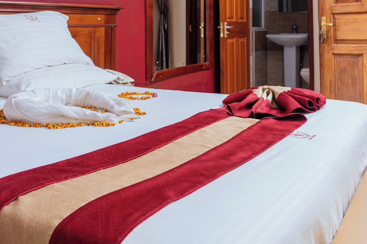 A hotel room with a bed, a red wall, a painting, and a bathroom visible through an open door.