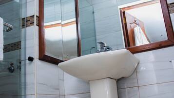 Un baño con cabina de ducha de vidrio, lavamanos sobre pedestal y espejo con marco de madera.