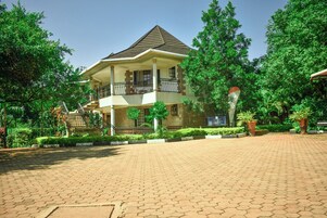 A two-story building with a balcony, surrounded by greenery and a paved walkway.