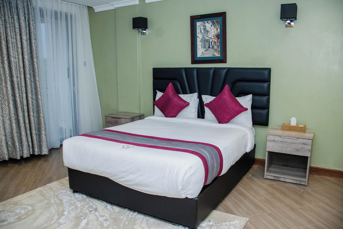 A neatly made bed with a headboard, a bedside table with a tissue box, and a framed picture on the wall.