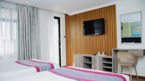 A hotel room with two beds, a TV mounted on the wall, a desk with a chair, and a wooden panel wall.