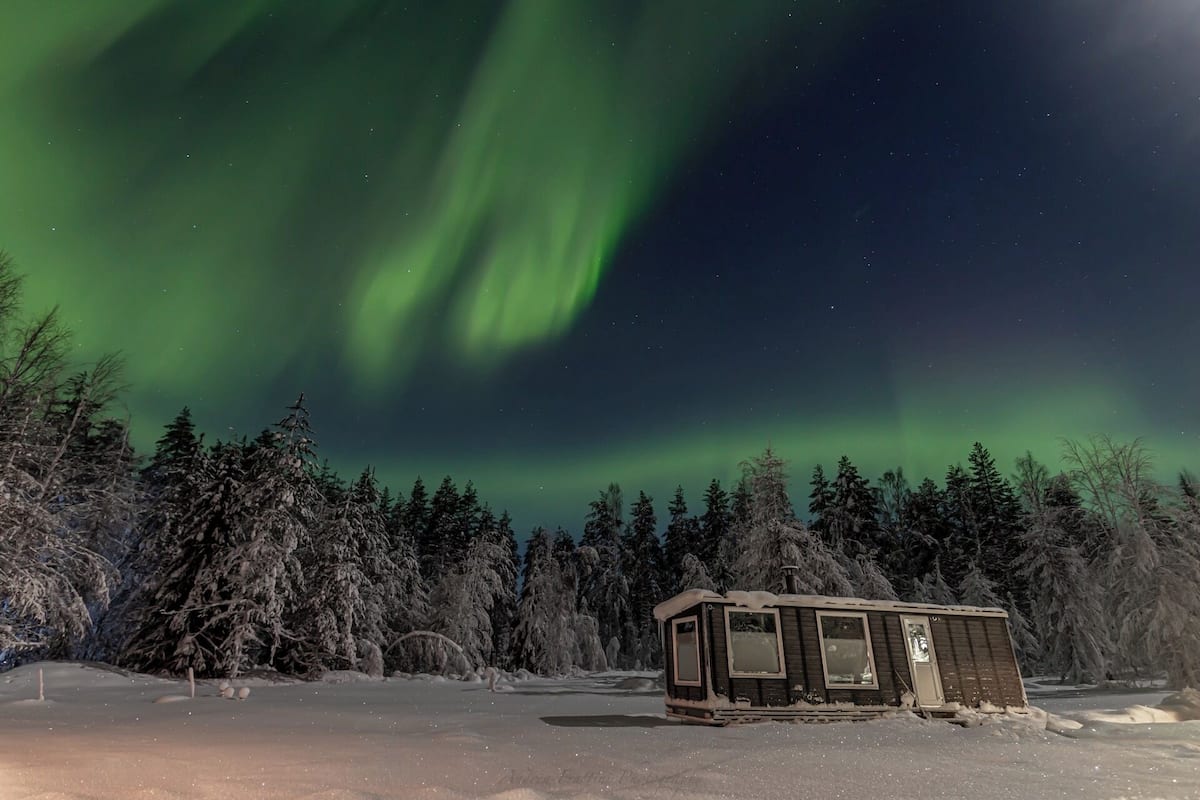 Una cabana petita en un bosc nevós amb vista a les Aurores Boreals.