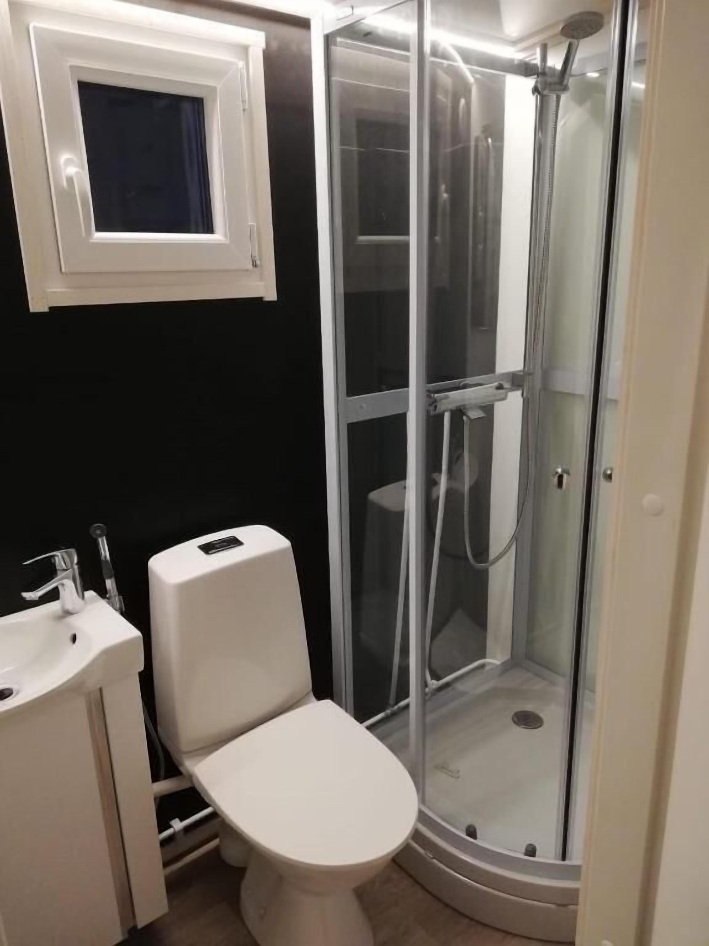 Kylpyhuone, jossa on wc, pesuallas ja lasiseinällä varustettu suihkutila.