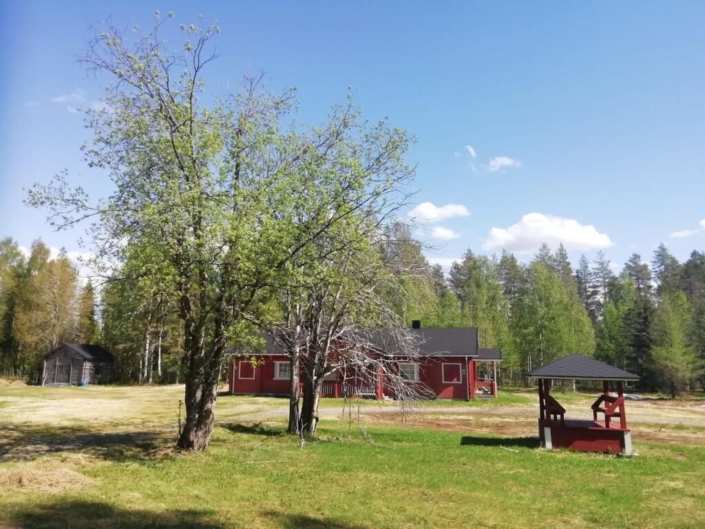 A red house with a porch and a small shed in a grassy area with trees.