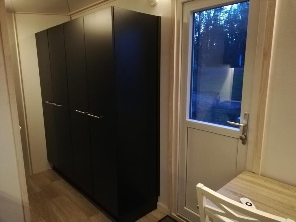 A room with a large wardrobe, a small table, and a window with a view of trees.