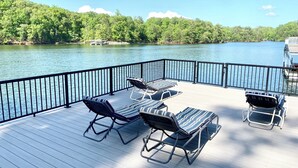 A deck with lounge chairs and a table overlooking a lake, surrounded by a metal railing.