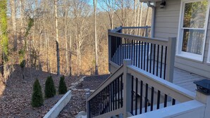 A residential deck with a railing, a stone pathway, and a forested background.
