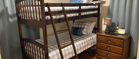 Un lit superposé avec une échelle, une table de chevet avec une lampe et une commode avec des tiroirs.