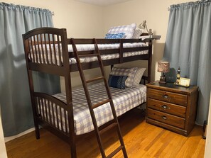A bunk bed with a ladder, a bedside table with a lamp, and a dresser with drawers.