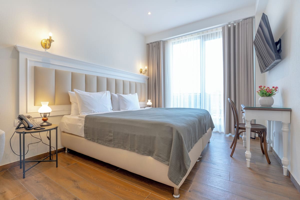 A neatly arranged hotel room with a bed, bedside table, lamp, and a small table with a vase.