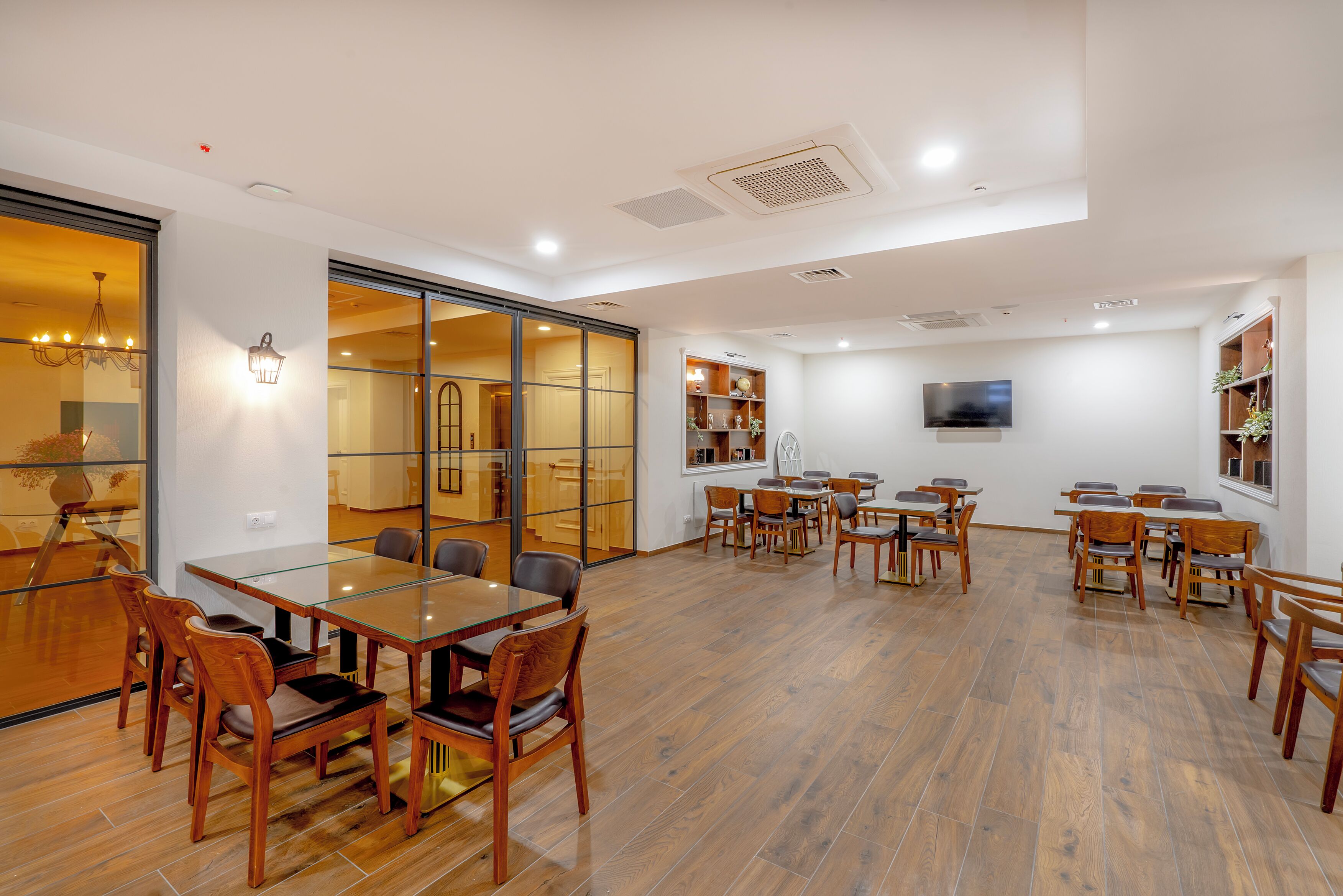 A spacious dining area with multiple tables and chairs, a large sliding glass door leading to another room, and a television mounted on the wall.