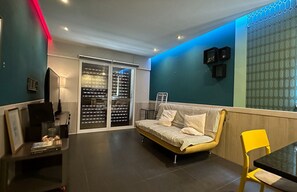 A modern living room with a sofa, a yellow chair, a TV, and a glass partition.