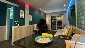 Uma sala de estar moderna com paredes verde-água, um sofá preto, uma poltrona amarela e uma área de jantar com bancada de granito e uma tigela de limões.