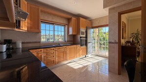 A modern kitchen with wooden cabinets, a large window, and a view of the outdoors. - Villa Sao Miguel (Albufeira)