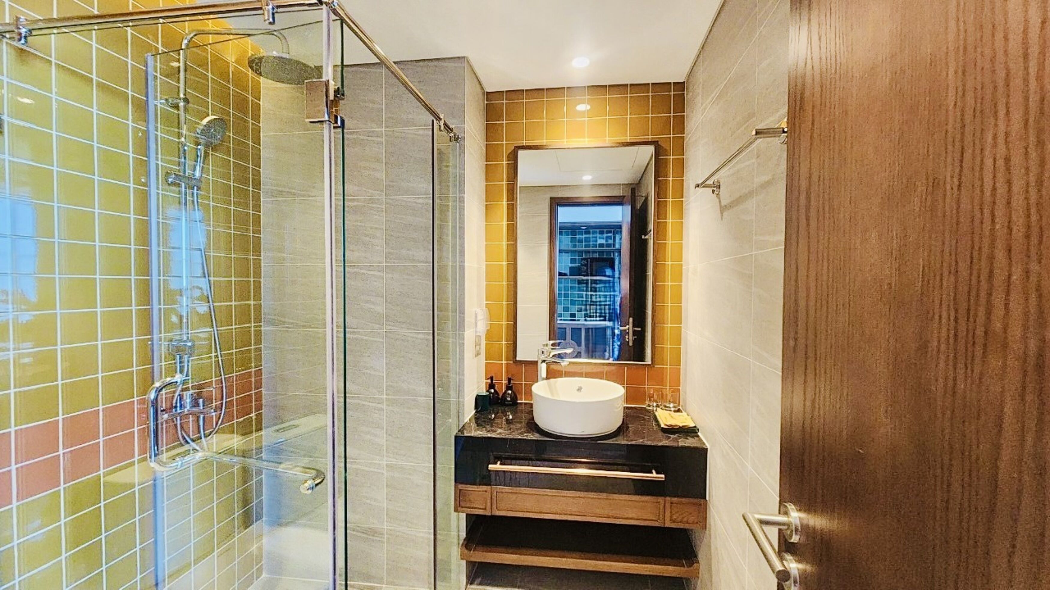 A bathroom with a glass shower enclosure, a sink with a mirror above it, and a wooden door.