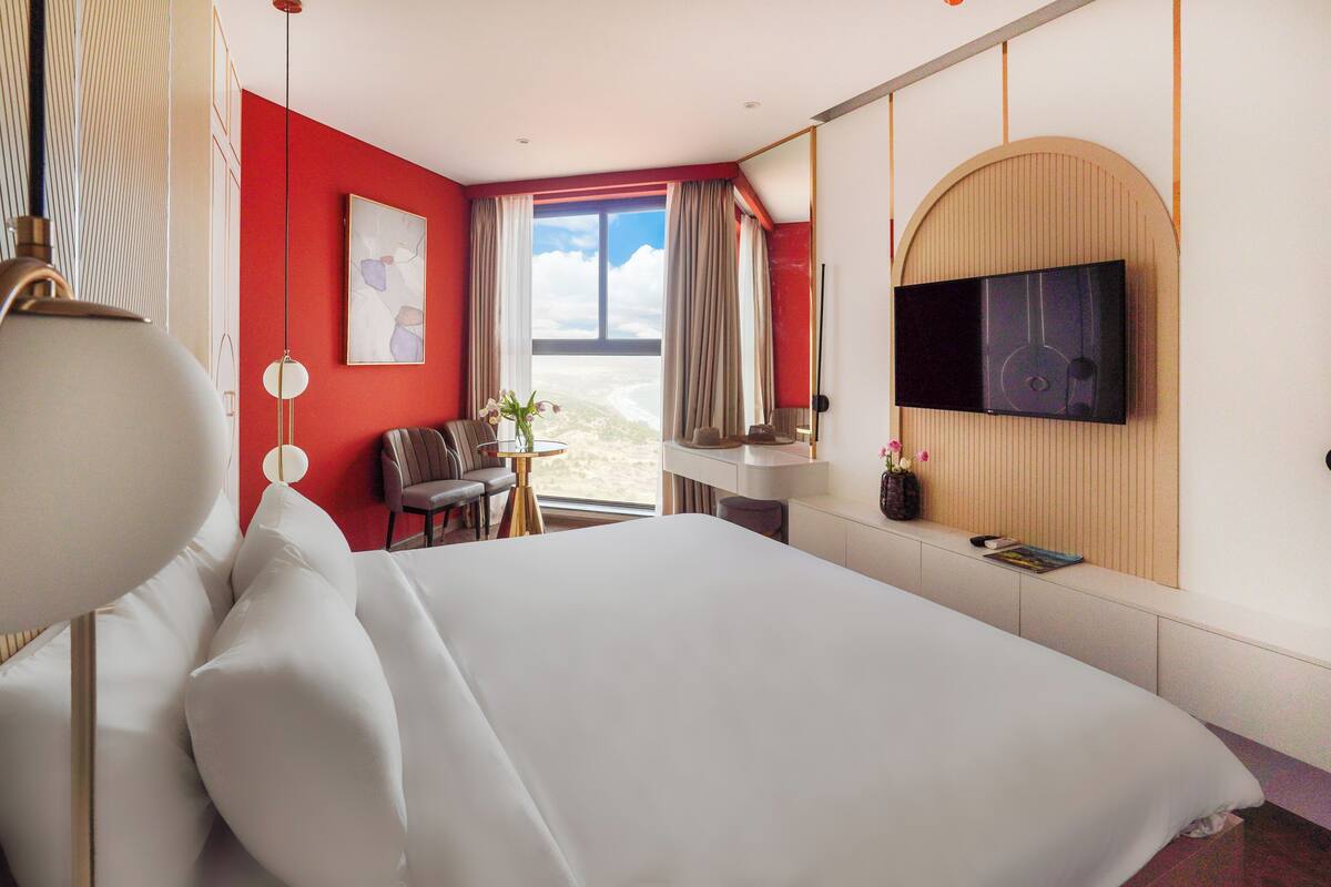 Une chambre d’hôtel avec un grand lit, un bureau avec une chaise, un téléviseur fixé au mur et une vue sur la plage.