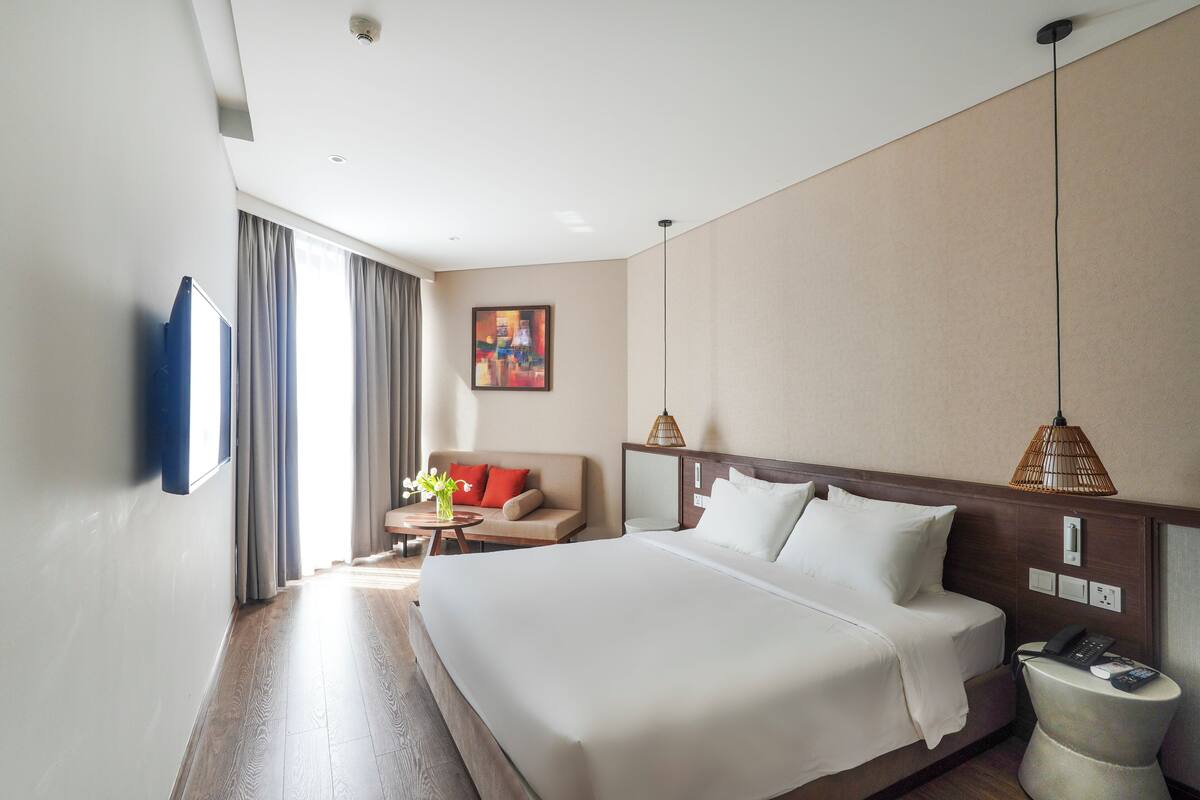 Une chambre d’hôtel avec un grand lit, un canapé, une petite table avec un vase et un tableau au mur.