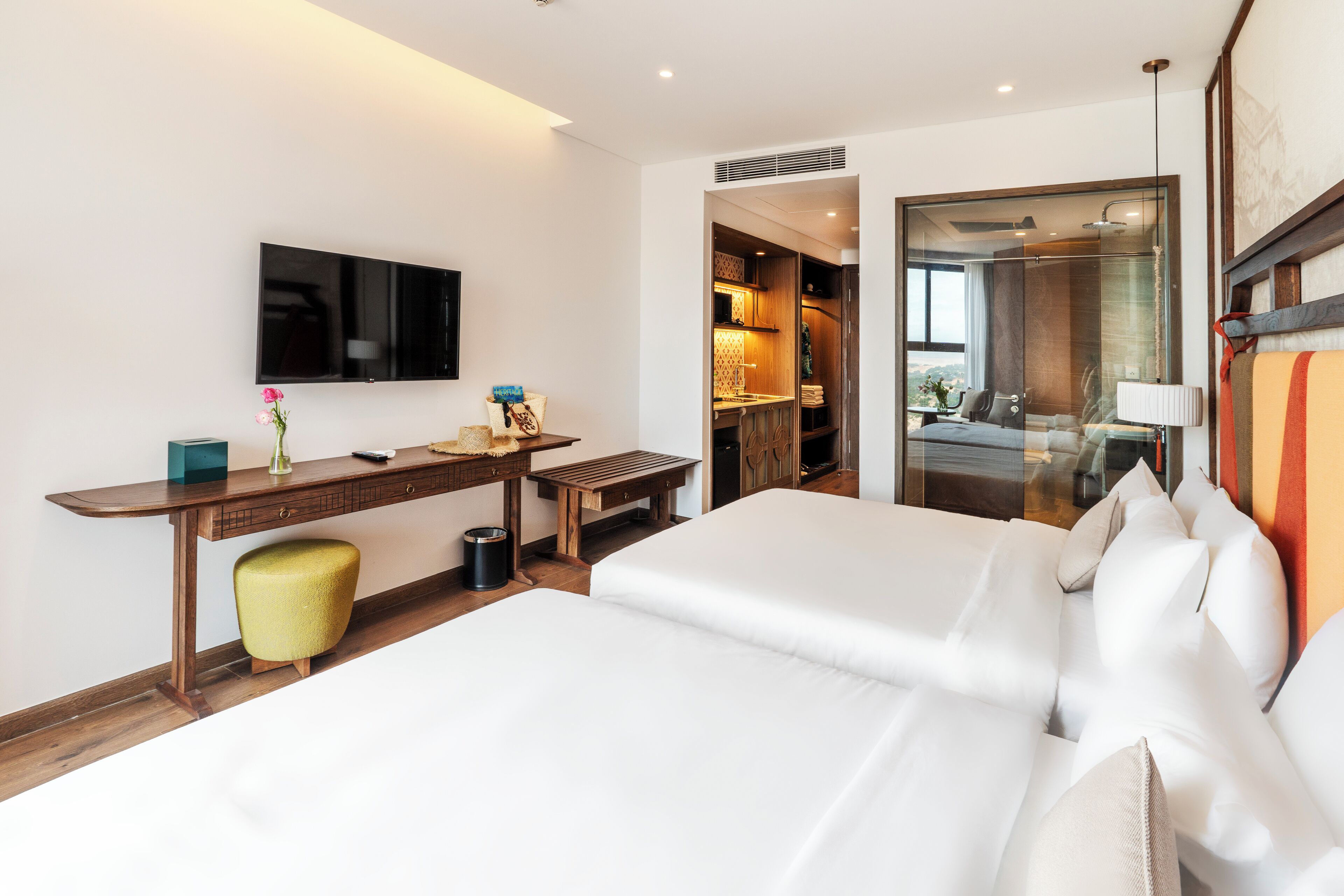 Hotelkamer met een bed, bureau, stoel, televisie en een badkamer zichtbaar door een glazen deur.