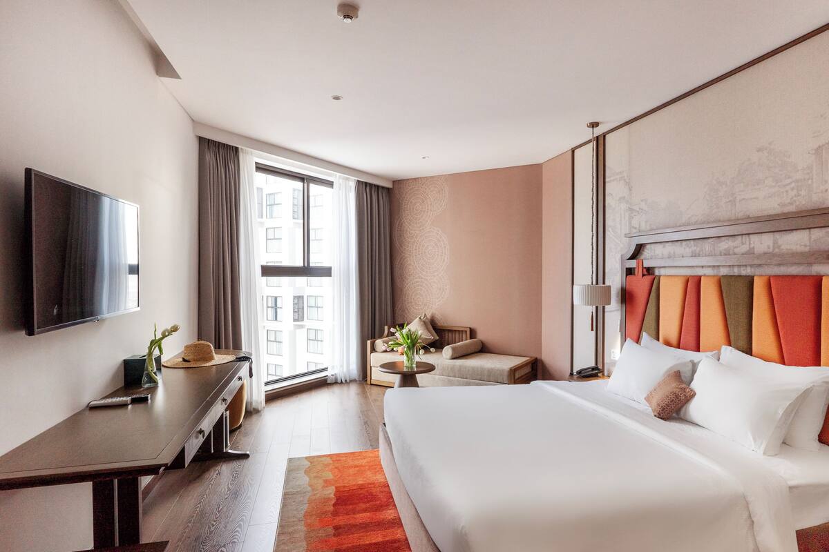 Une chambre d’hôtel avec un grand lit, un bureau avec une télévision, un canapé et une fenêtre avec des rideaux.