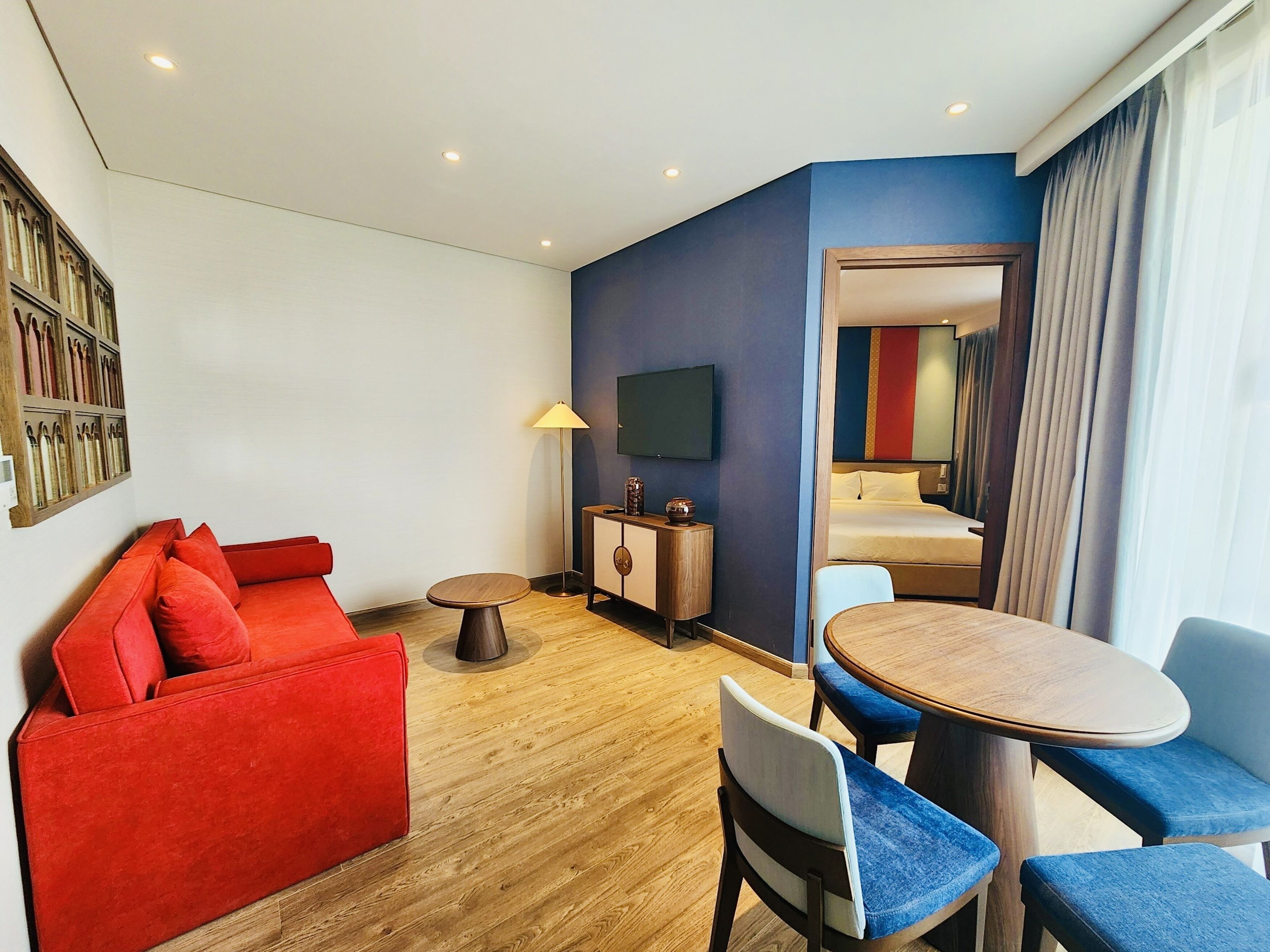 Una camera d'albergo con un divano rosso, un tavolino rotondo in legno, una TV e un letto con tende.
