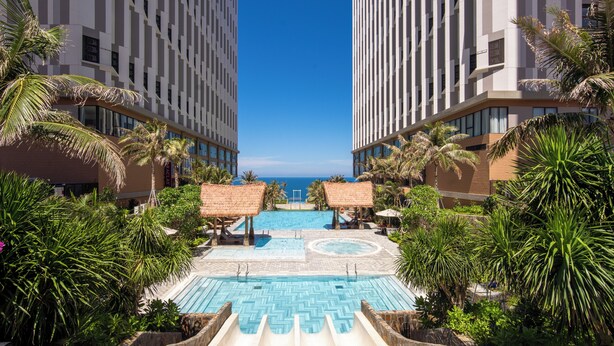 A resort pool area with a clear view of the ocean, surrounded by palm trees and modern buildings. - Sunrise By Mandala Mui Ne (Mui Ne)