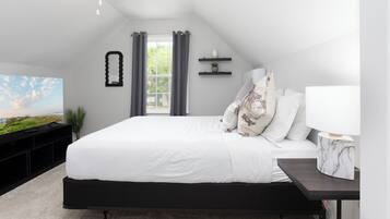 Quarto com cama grande, televisão, mesinha e janela com cortinas.